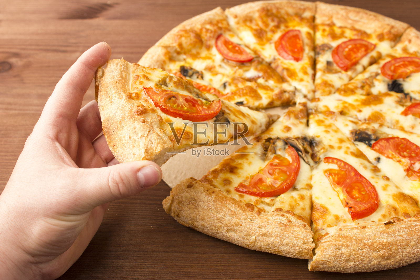 手里拿着一块美味的披萨。蘑菇披萨配奶酪和西红柿照片摄影图片