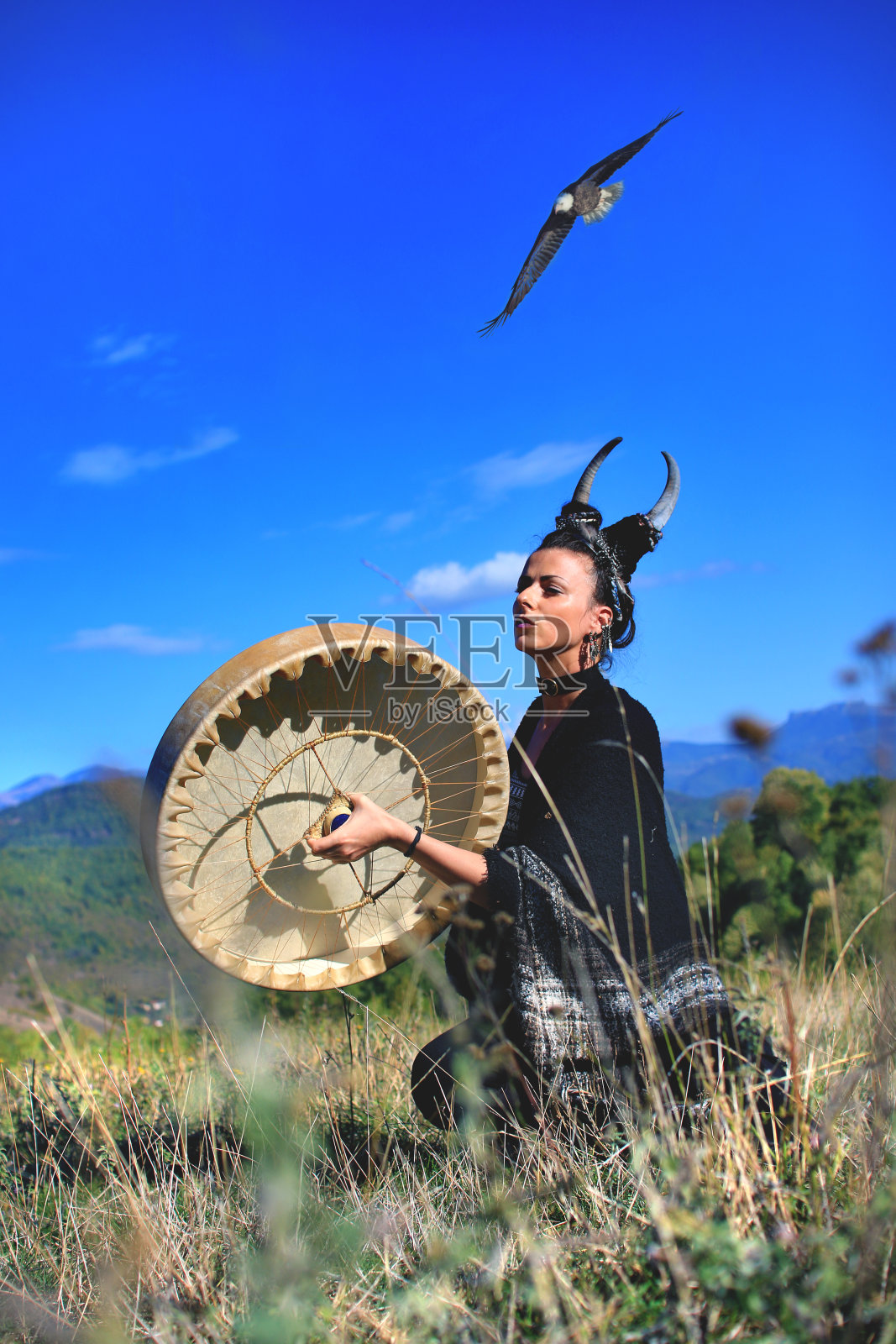 部落异教妇女用鹿角在山上敲着水牛萨满鼓照片摄影图片