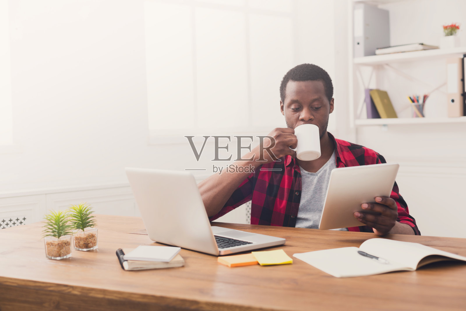 黑人商人在休闲办公室里，在平板电脑上看新闻，喝酒照片摄影图片