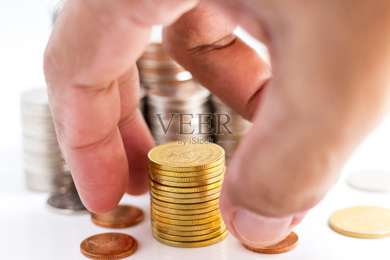 金币摞起来，手放在白色的桌子上。照片摄影图片