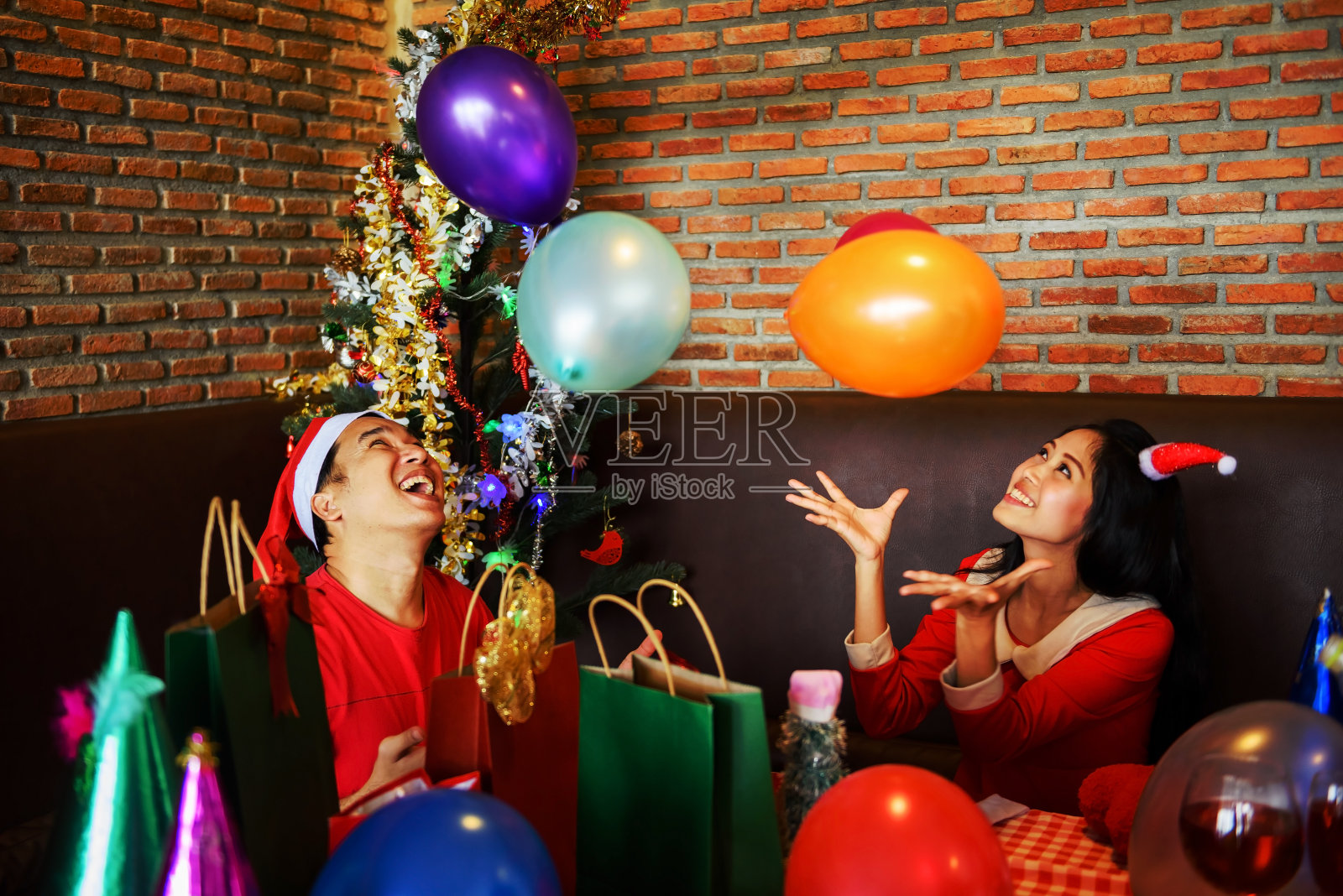 年轻的亚洲幸福的男女夫妇与圣诞老人帽子玩和扔彩色的玩具气球为圣诞节或圣诞和新年庆祝派对酒吧照片摄影图片