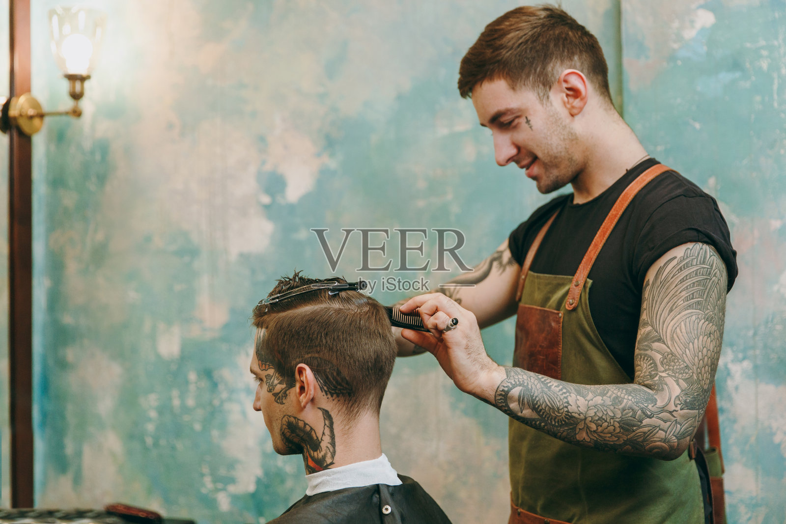 近距离拍摄的男人得到时髦的发型在理发店。男性发型师在纹身服务客户。照片摄影图片