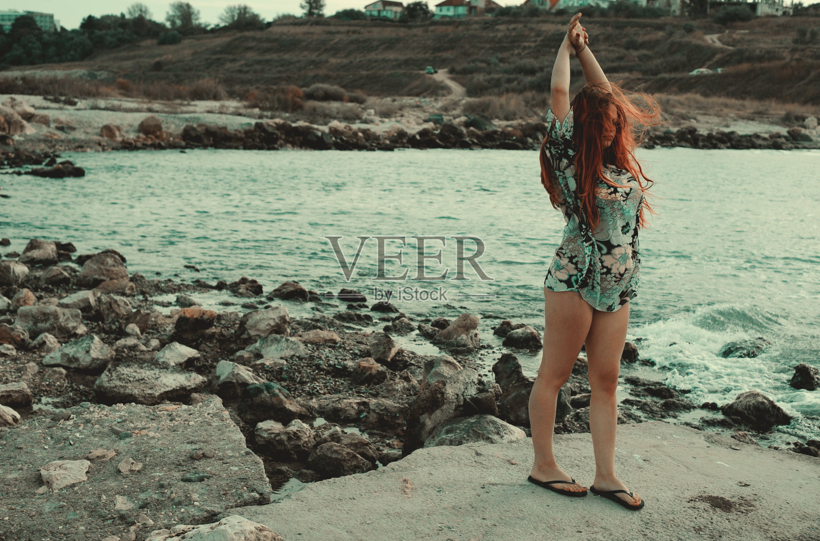 美丽的女孩在海边的岩石上休息。照片摄影图片