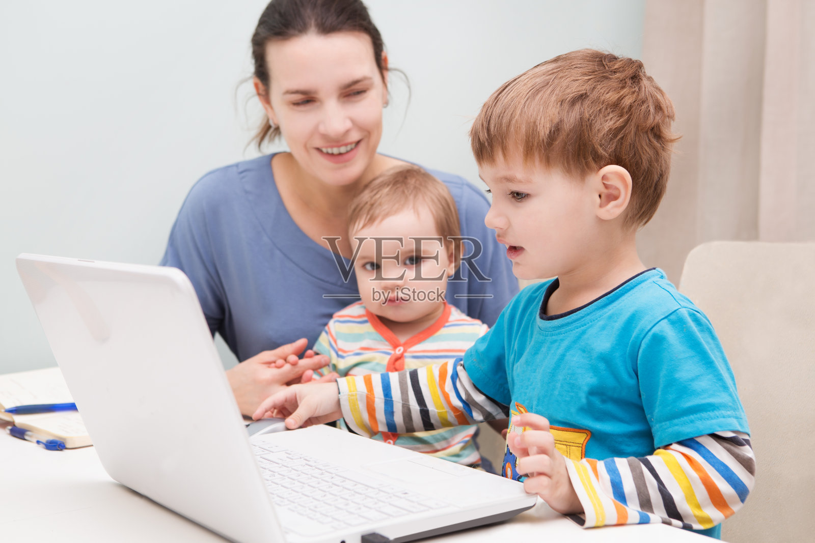 一个母亲在家工作，养育她的两个孩子。照片摄影图片