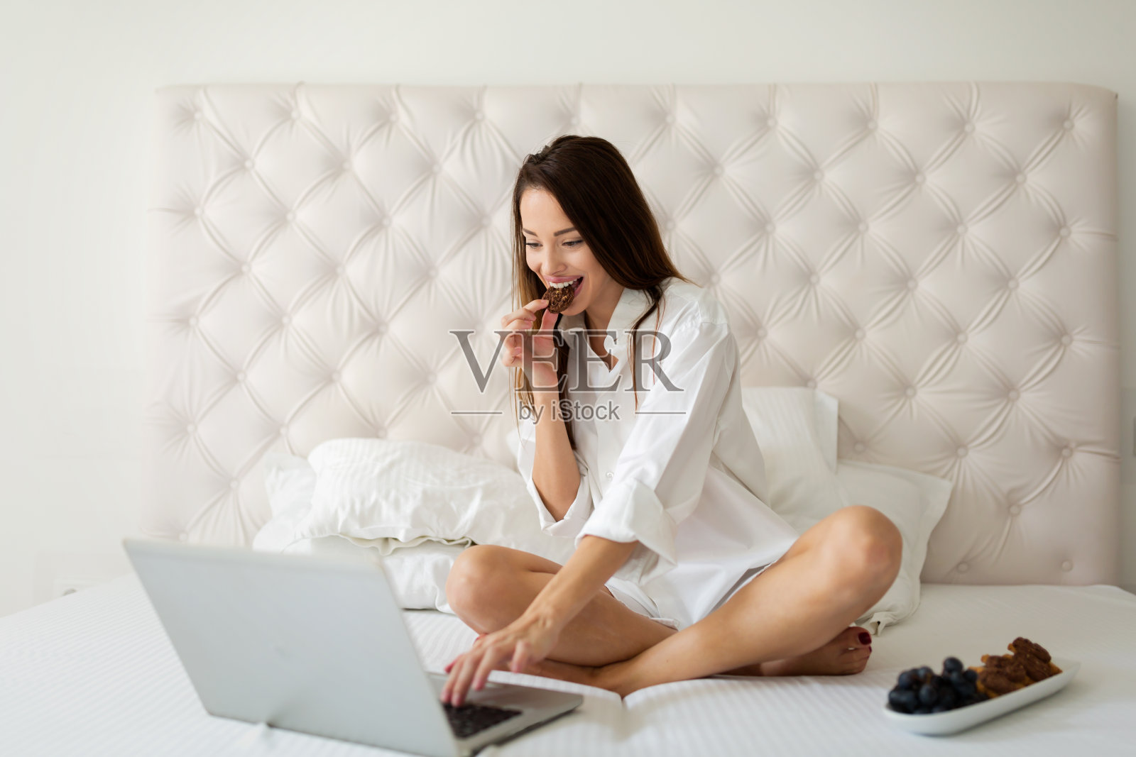 年轻女子坐在床上吃饼干和使用电脑照片摄影图片