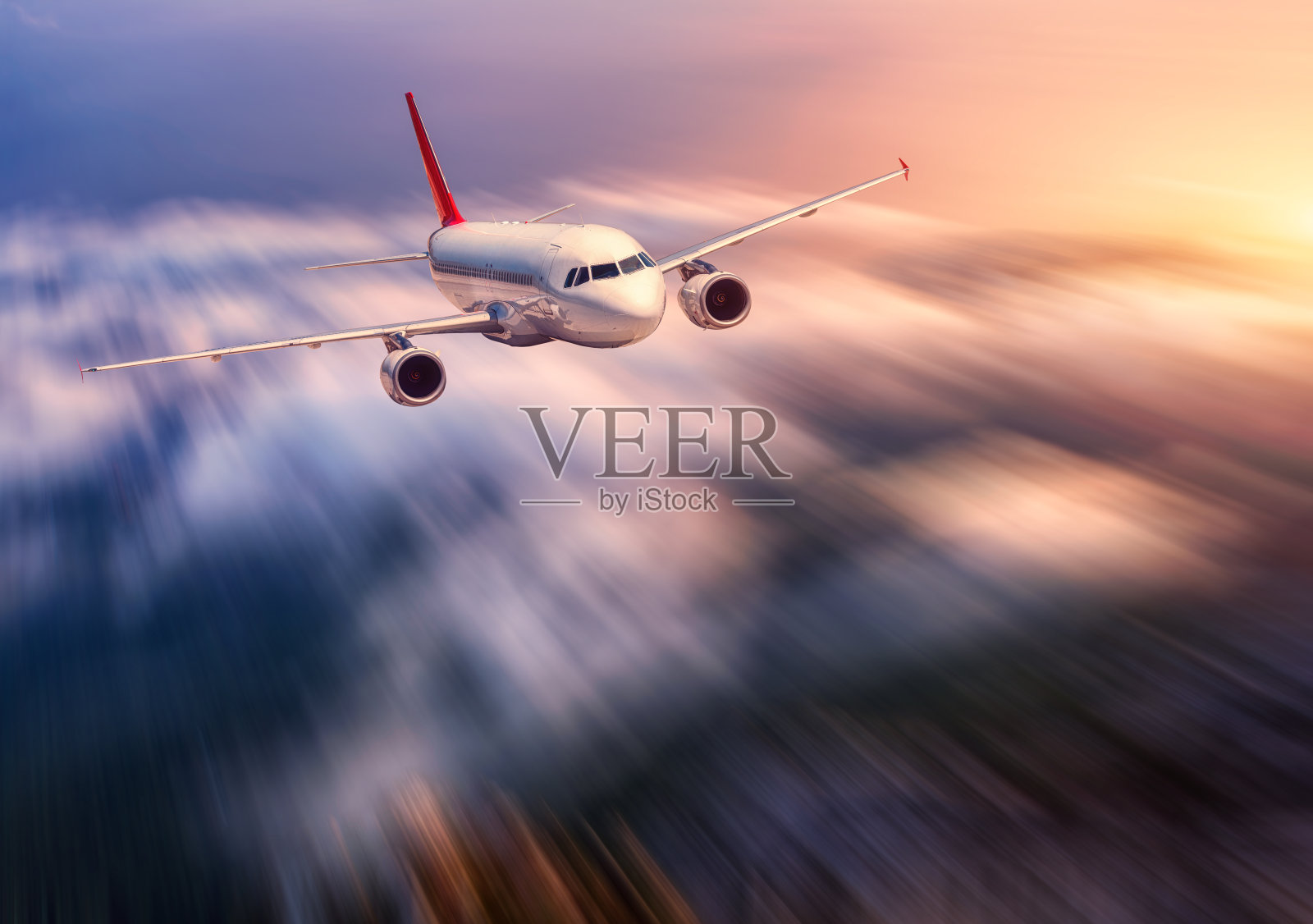 现代飞机的运动模糊效果是在日落低云上空飞行。有飞机的风景，模糊的云，黄昏的阳光。客机。商务旅行。商用飞机照片摄影图片