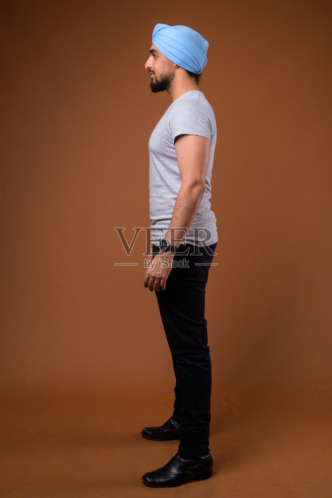 一名留着胡子的年轻印度男子穿着休闲服装，头戴蓝色头巾，背景是彩色的照片摄影图片