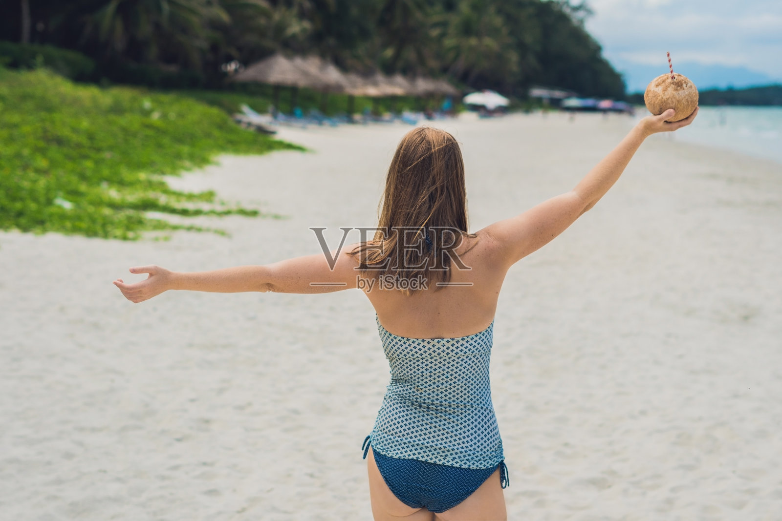 年轻女子在海滩上喝椰奶。照片摄影图片