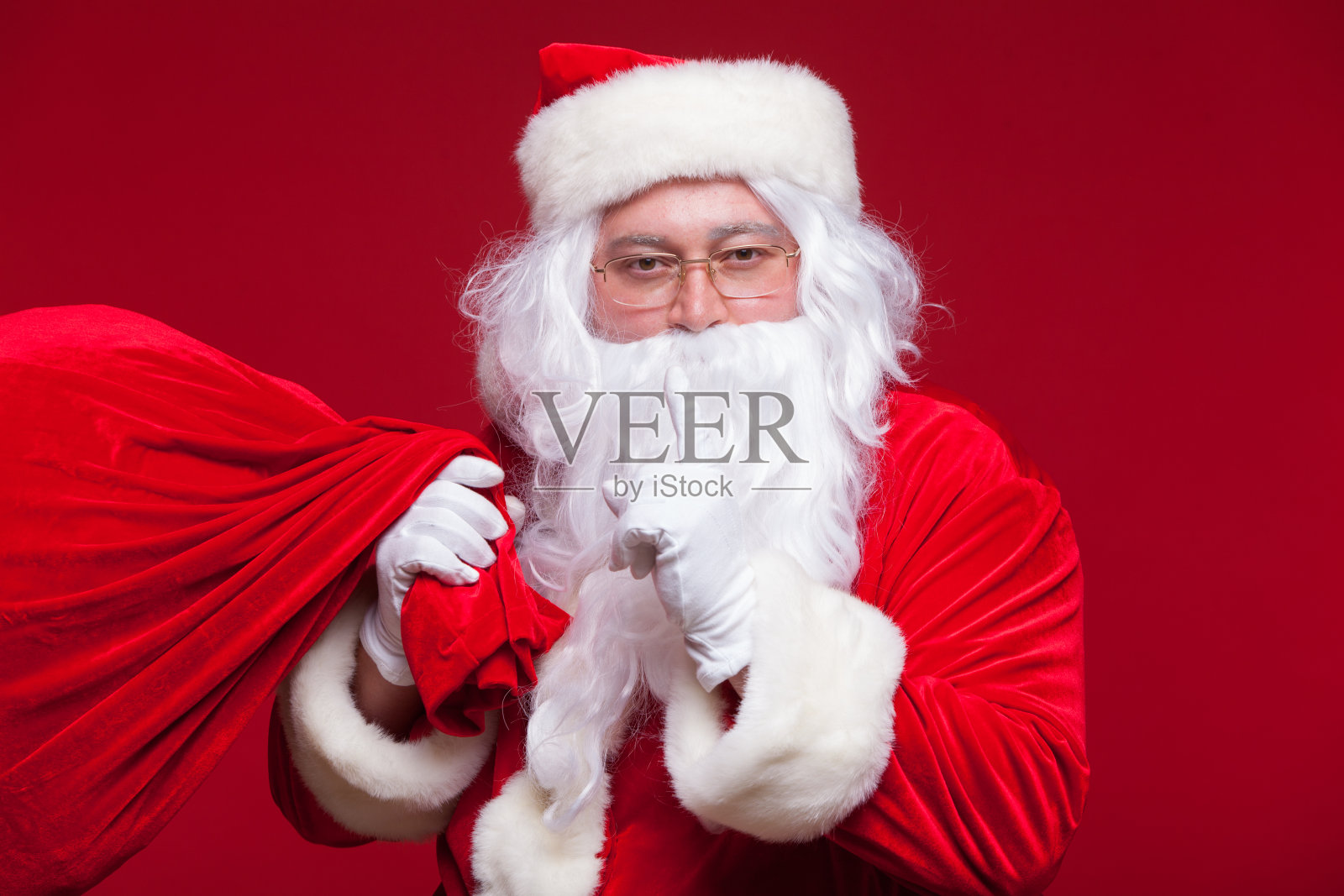 圣诞老人的肖像与巨大的红色口袋保持食指对着他的嘴和镜头照片摄影图片