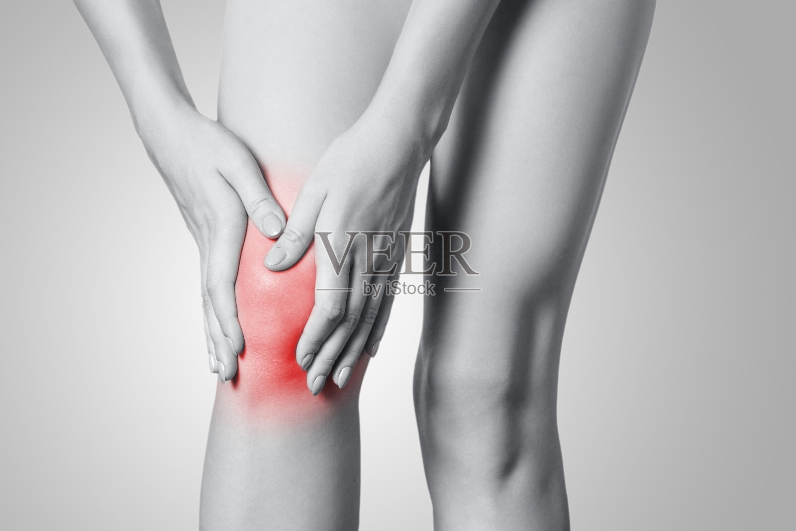 一个年轻女人的膝盖疼痛的特写在灰色的背景。照片摄影图片