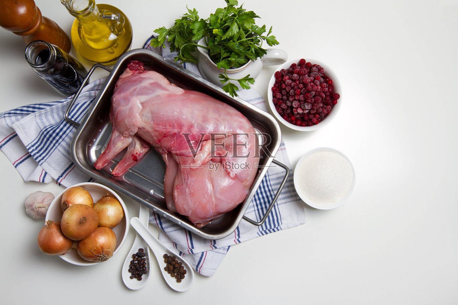生兔肉，洋葱，大蒜，欧芹，蔓越莓，糖，多香果和杜松子放在白色的桌子上照片摄影图片