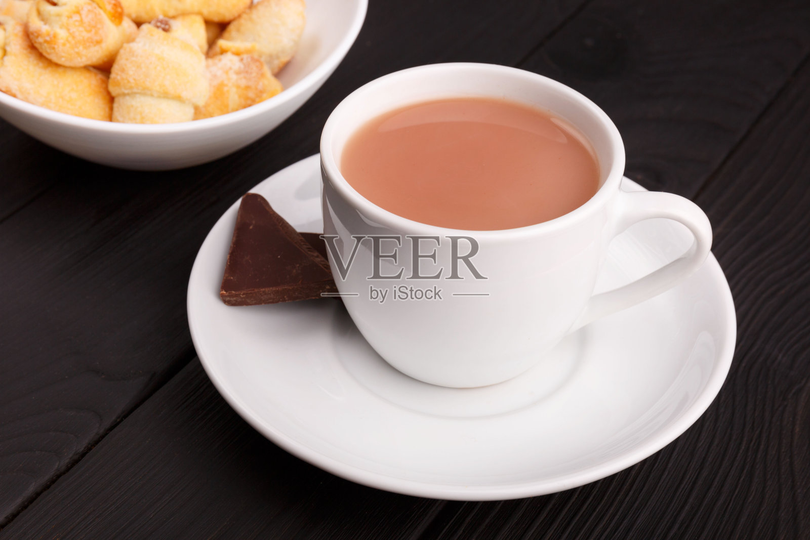 茶托上放着一杯牛奶茶和一盘小卷饼。在一个表。照片摄影图片