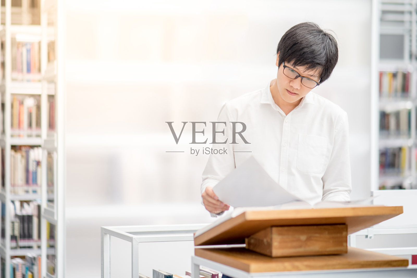 年轻的亚裔大学生在图书馆的讲台上阅读推荐的书照片摄影图片