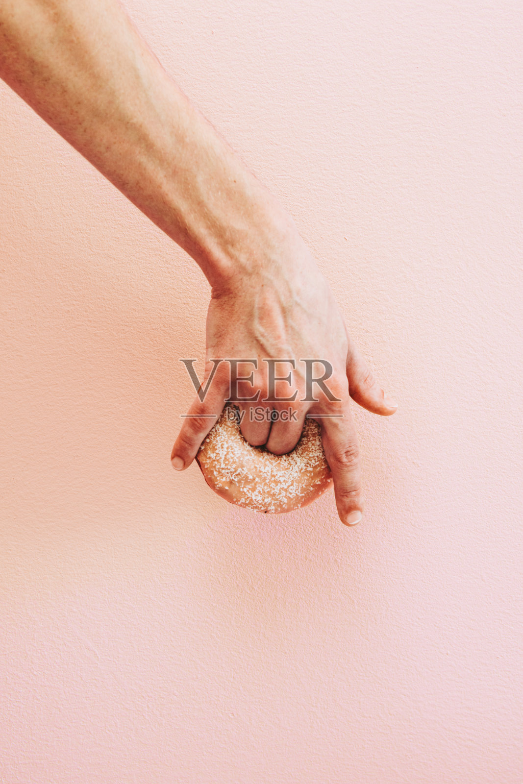 手拿着甜甜圈靠在粉红色的墙上。照片摄影图片