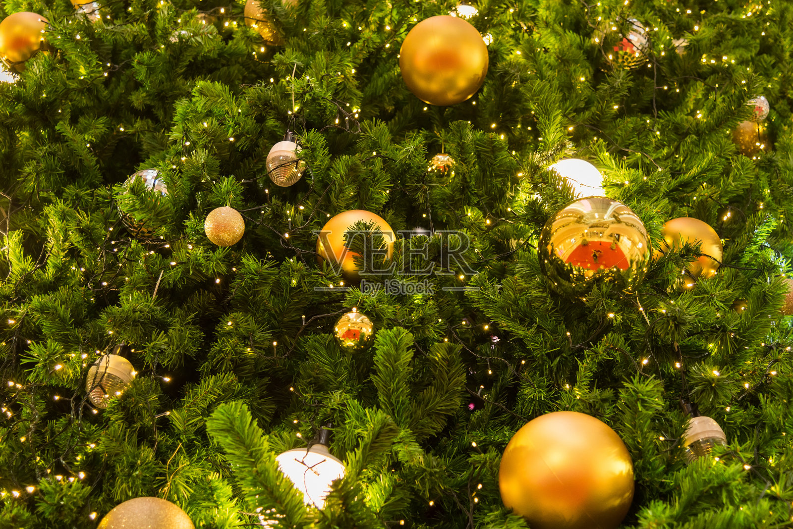 许多镜子球装饰在绿色的树叶，树和照明系统在百货公司的问候季节，如圣诞节和新年节日。散景灯背景在圣诞节。照片摄影图片