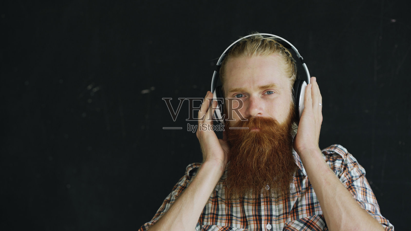 这是一个留着胡子的年轻人的特写，他戴着耳机听着音乐，微笑着看着镜头照片摄影图片