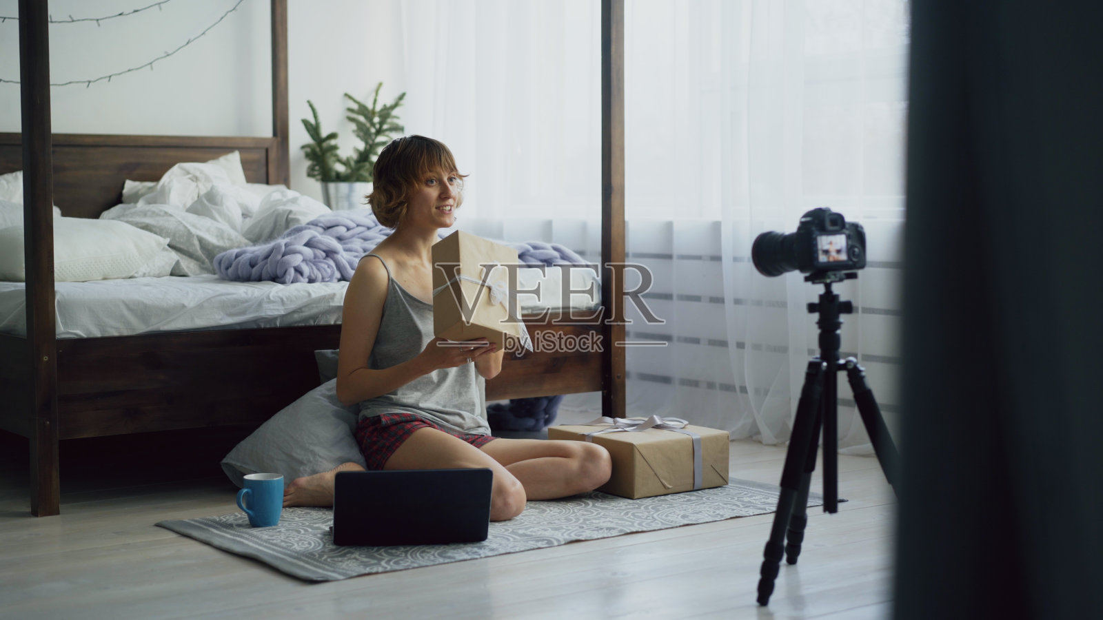 迷人的年轻女子坐在床边录制视频博客关于包装礼盒与单反相机照片摄影图片