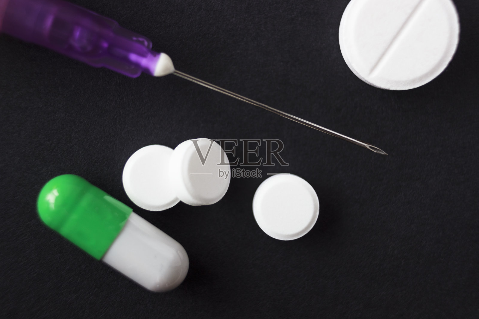 注射器的针放在药片中间，在黑色的背景上，宏照片摄影图片