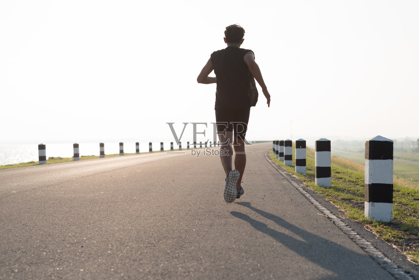 亚洲青年男子在日出的时候在大坝公路上跑步锻炼。健康的生活方式照片摄影图片
