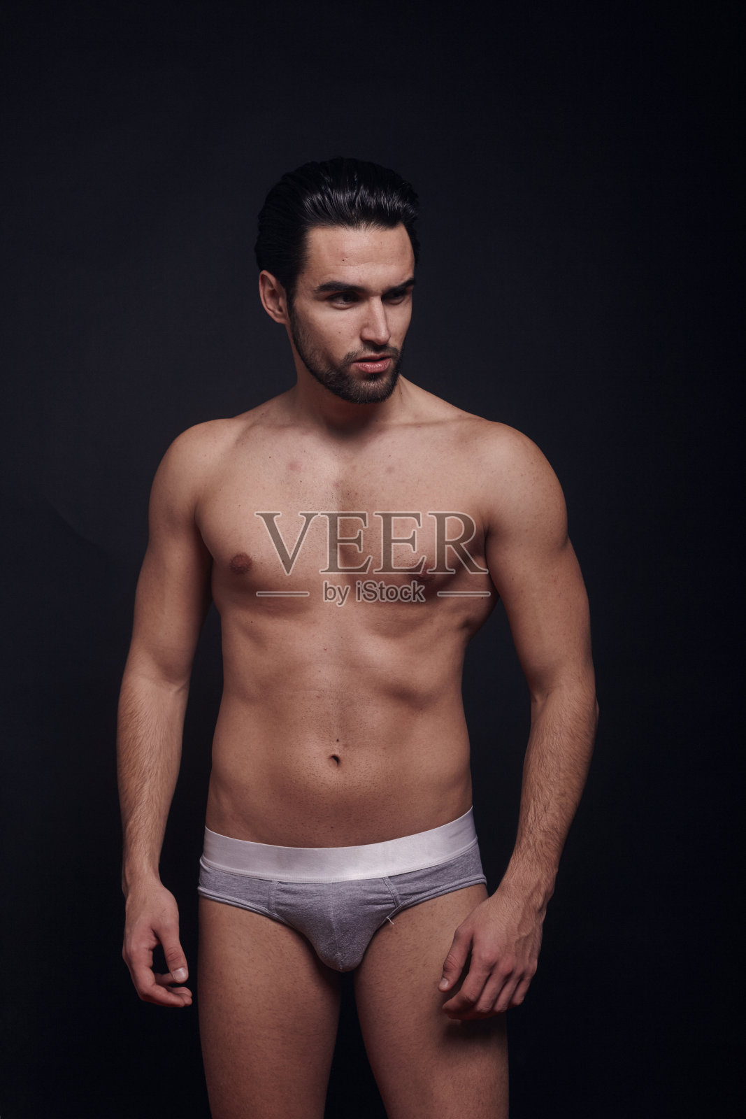 一个年轻帅气的男子，目光远离镜头，赤膊，时尚模特，黑色背景穿着内裤。照片摄影图片