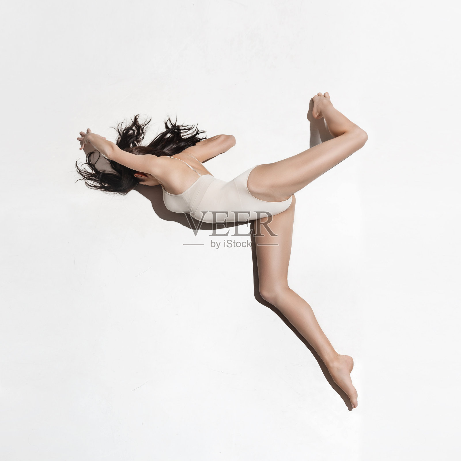 年轻美丽的舞者在米色连衣裙上跳舞在灰色的背景照片摄影图片