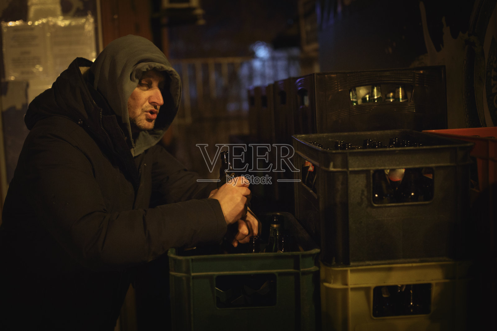 寒冷的冬夜，醉酒男子在户外喝啤酒照片摄影图片