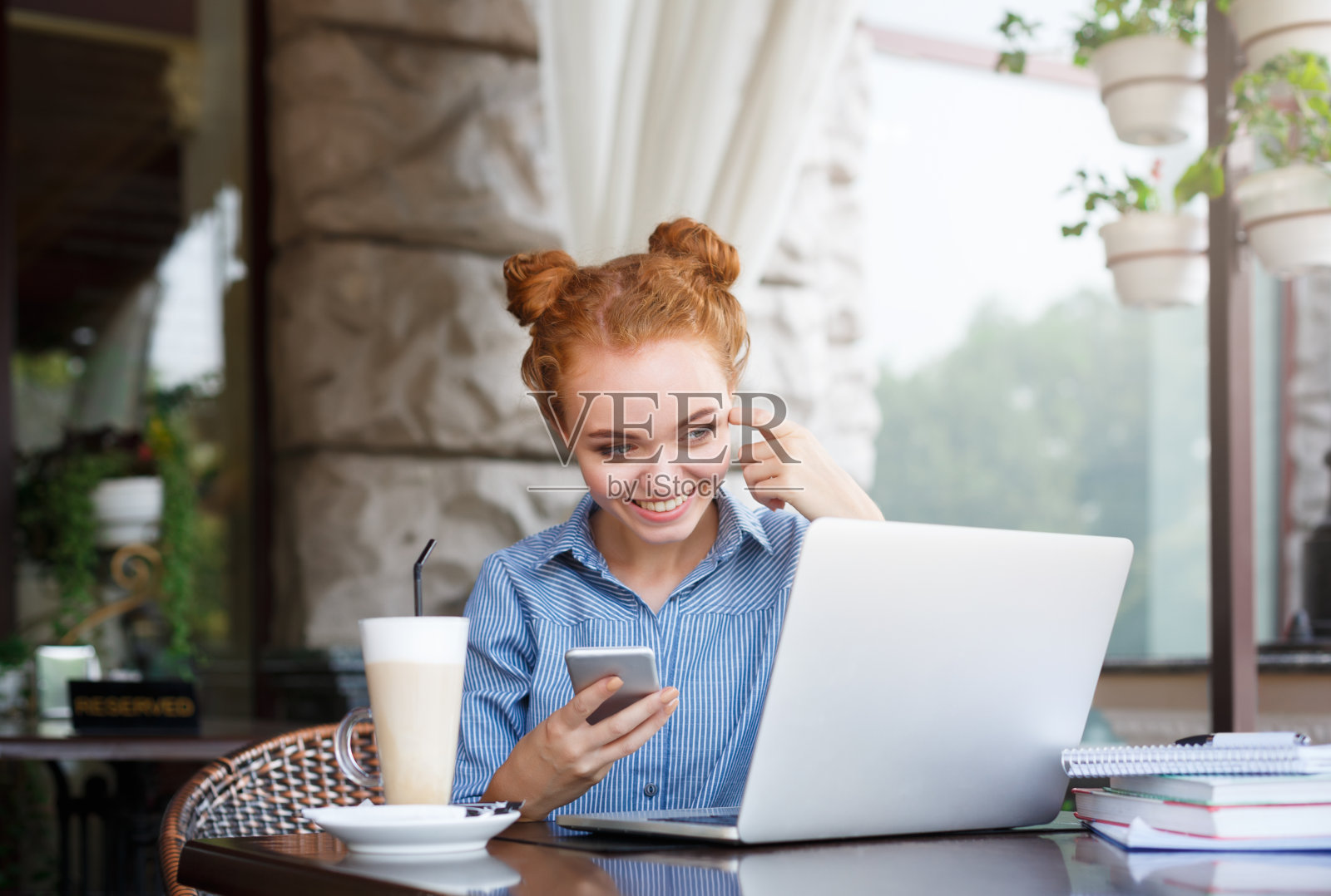 年轻的红发女人看着笔记本电脑，拿着手机照片摄影图片