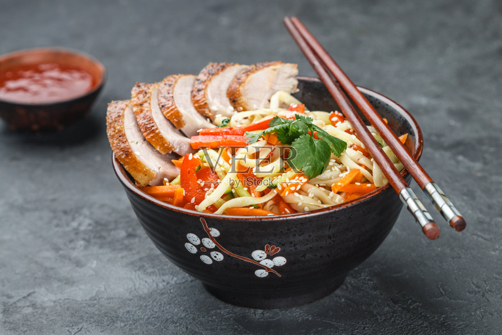 乌冬面配蔬菜(胡萝卜，辣椒，西葫芦，黄瓜，洋葱，香菜，大蒜)，鸭子和芝麻。炒菜。有选择性的重点照片摄影图片