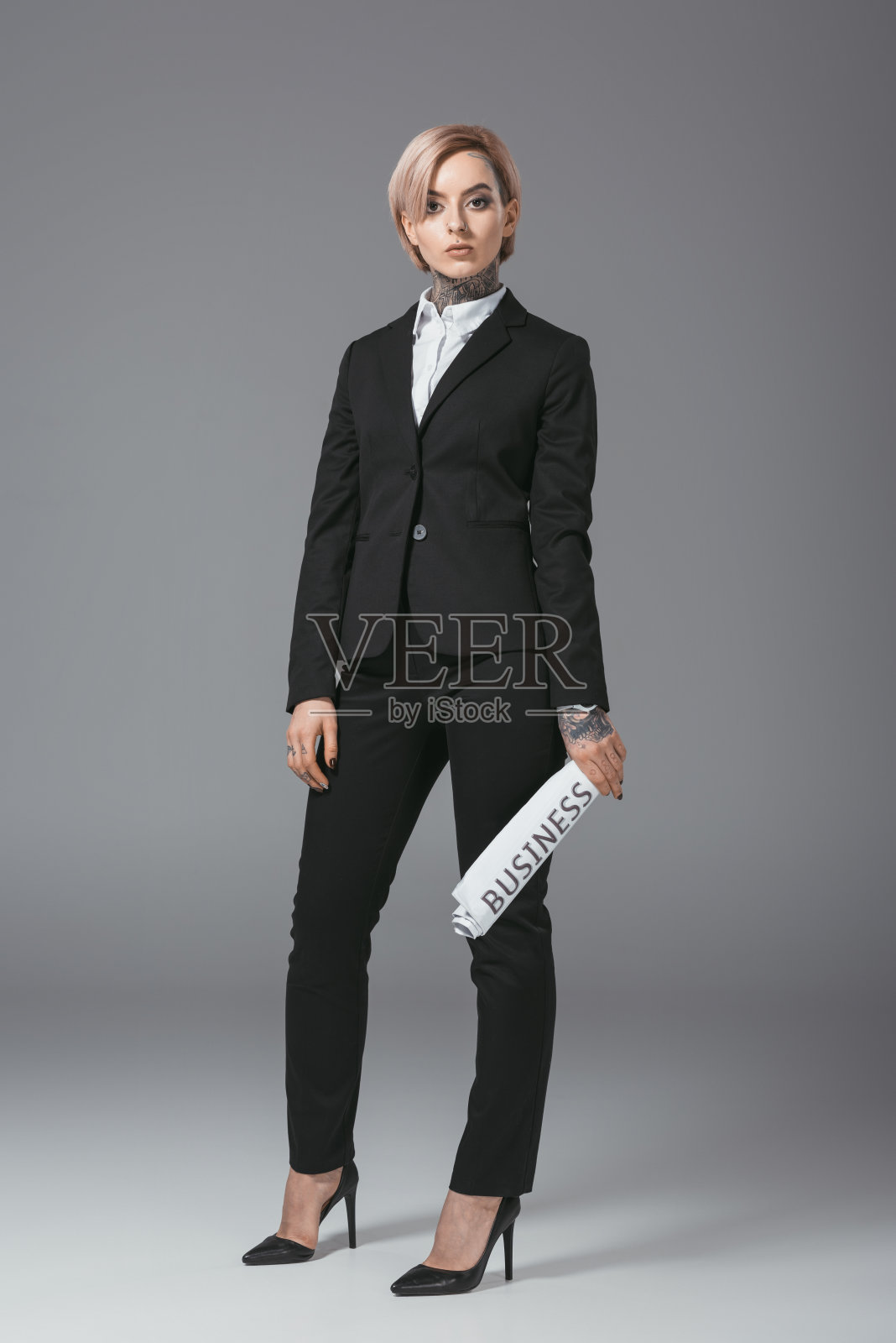 美丽的女商人与粉红色的头发在西装拿着报纸，孤立在灰色照片摄影图片