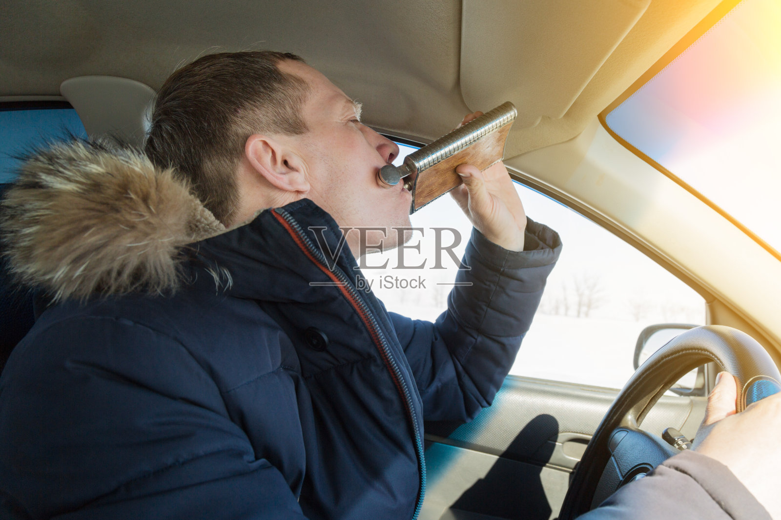 酒鬼的司机在开车时喝白兰地。照片摄影图片