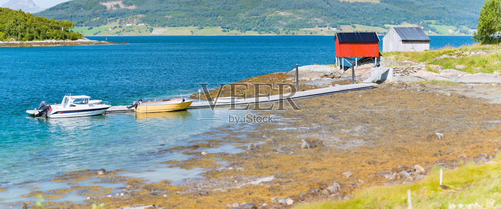 挪威美丽的风景。红色的谷仓，树木和水，山的背景。去欧洲的斯堪的纳维亚半岛旅行。船在码头。照片摄影图片