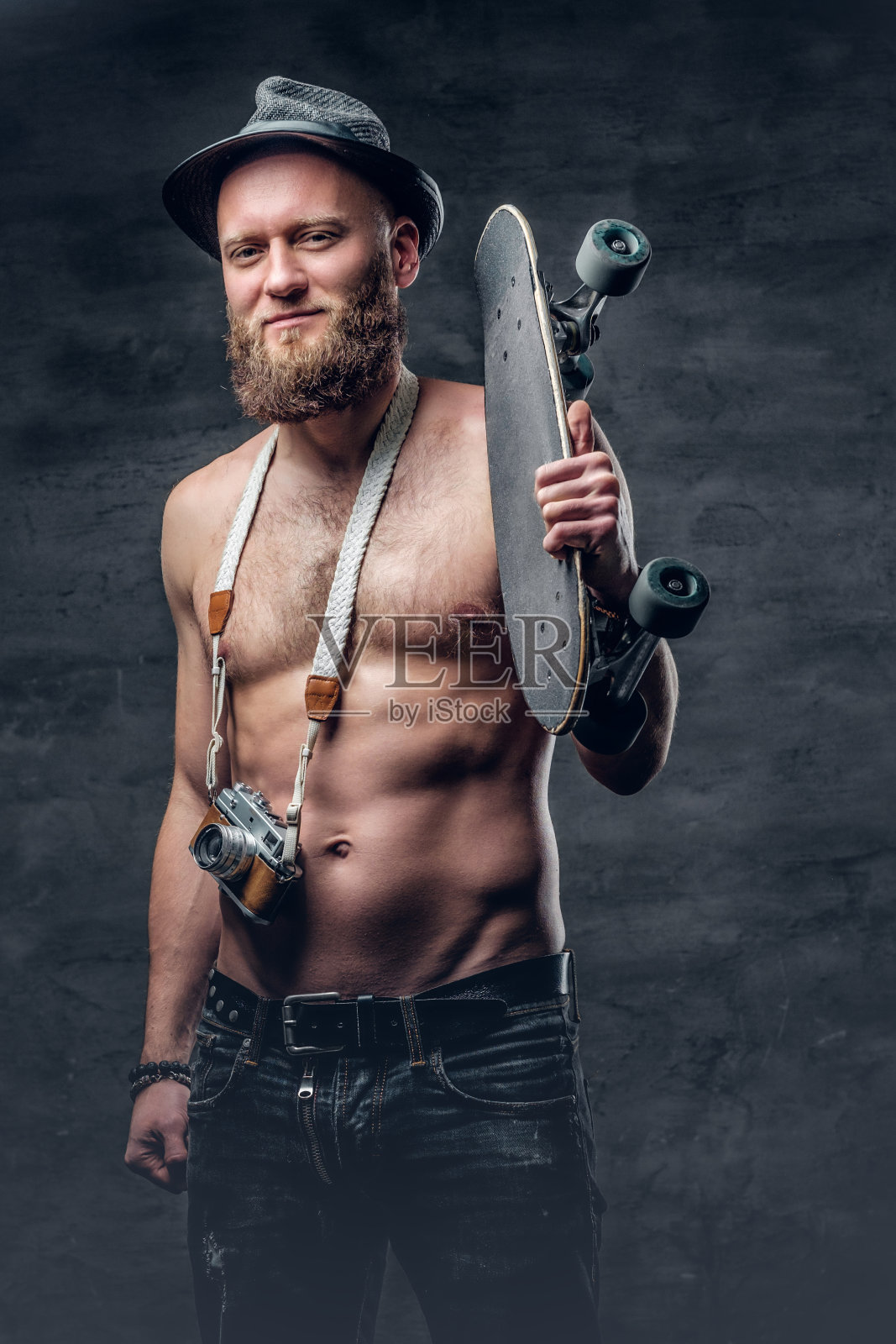 这名蓄着胡须的赤膊男子手持滑板。照片摄影图片