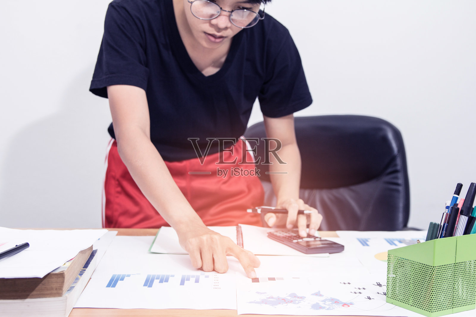 亚洲年轻女子在黑衬衫拿笔工作，计算税导致清算，与日落光复古风格。照片摄影图片