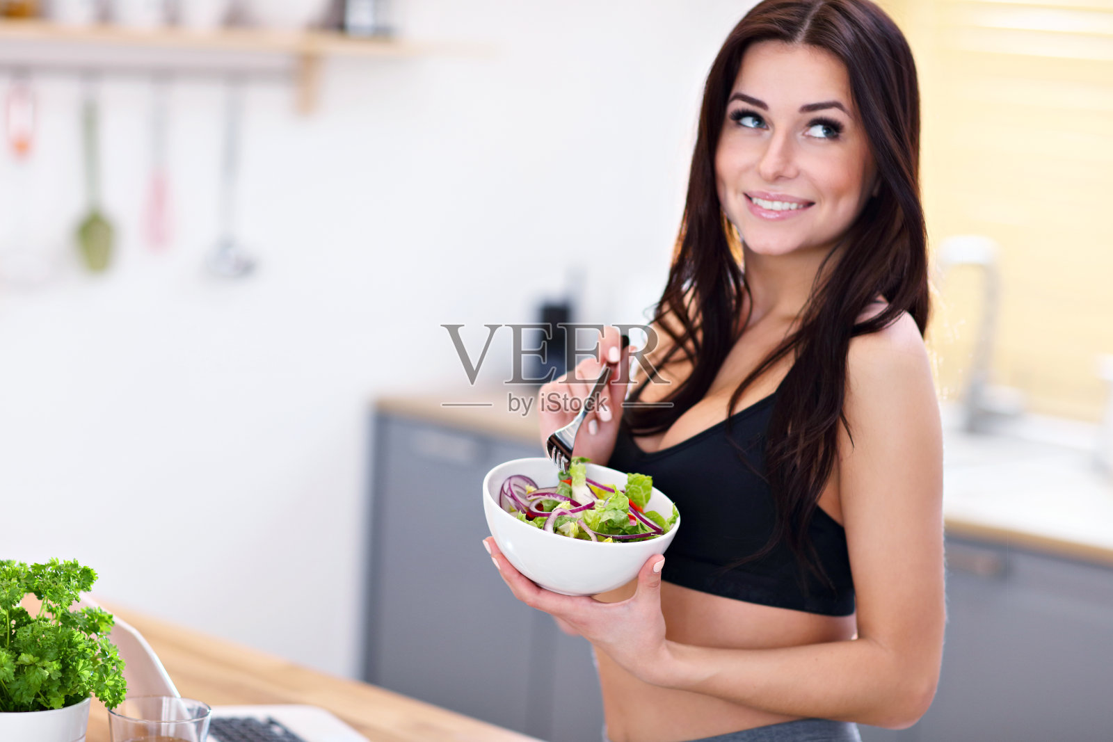 在现代化的厨房里，笑容灿烂的年轻女子正在吃沙拉照片摄影图片