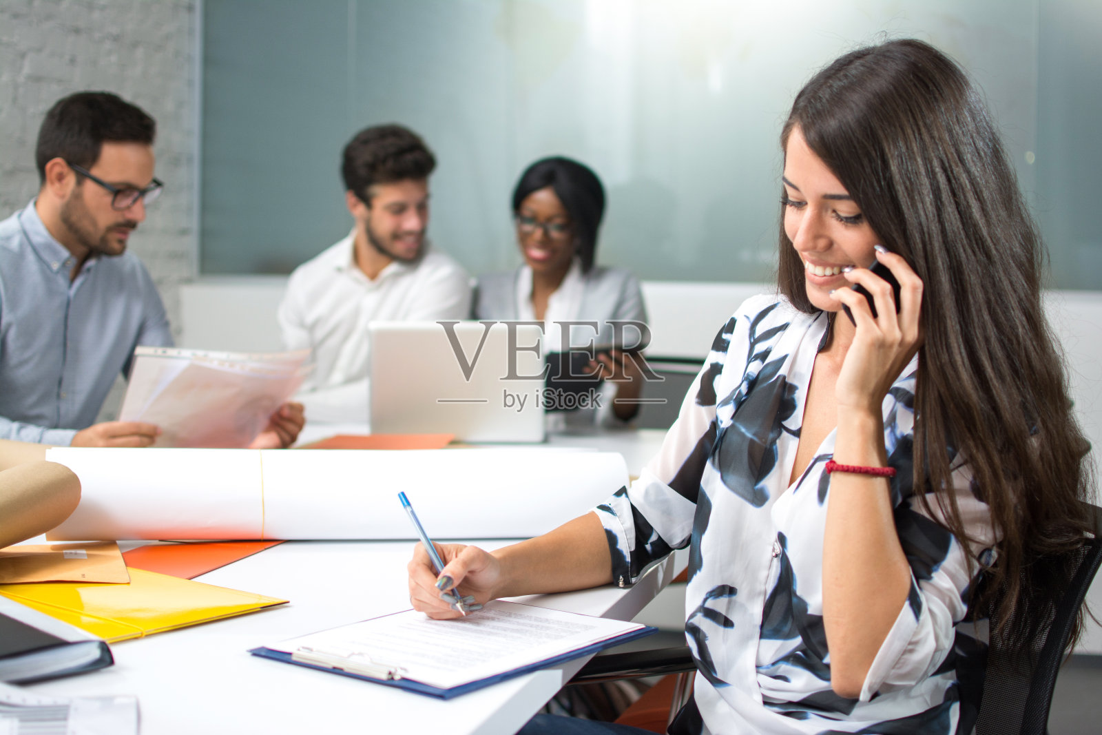 微笑的商务女性打电话和在工作场所的剪贴板上写笔记照片摄影图片