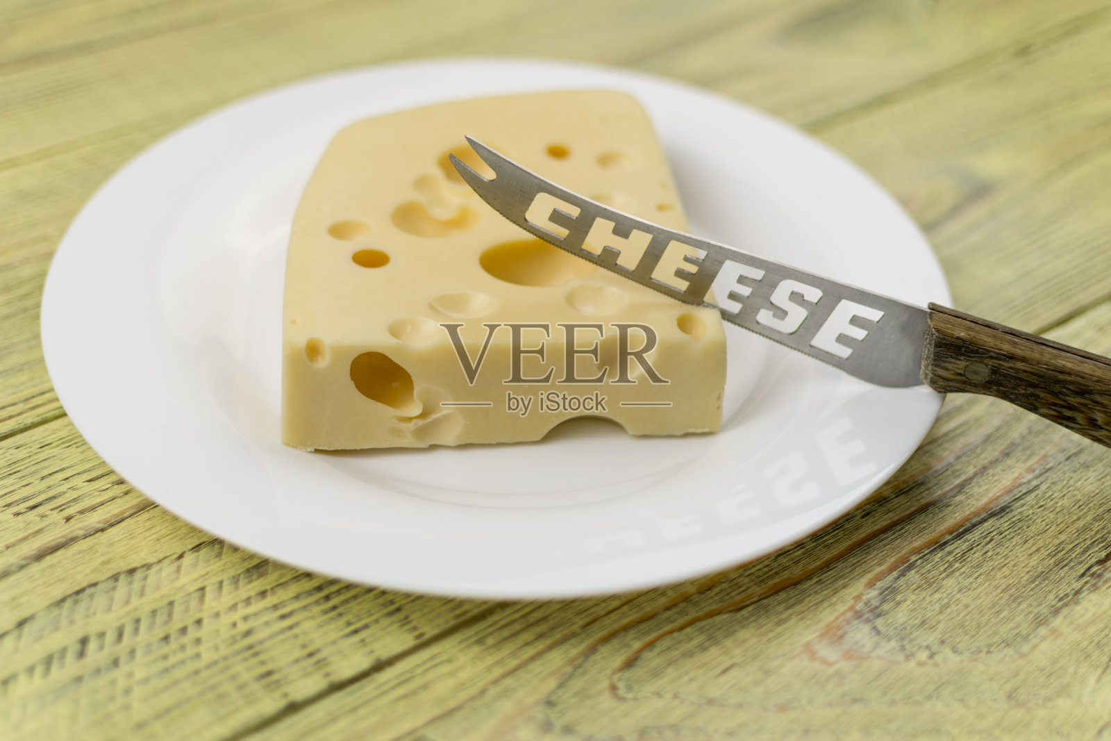 白色盘子上有孔的奶酪和用来切东西的刀。照片摄影图片