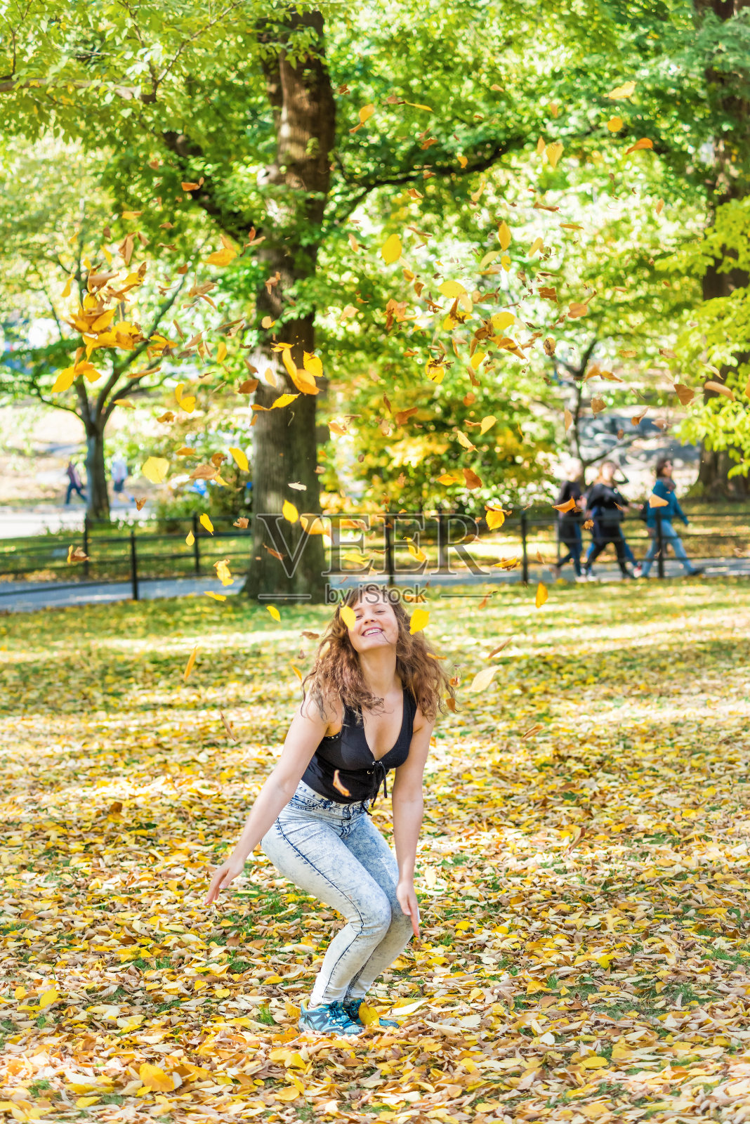 曼哈顿纽约市中央公园，年轻的潮女千禧跳，快乐的微笑许多落叶在空中飘落在秋天的秋天季节与黄色的树叶照片摄影图片