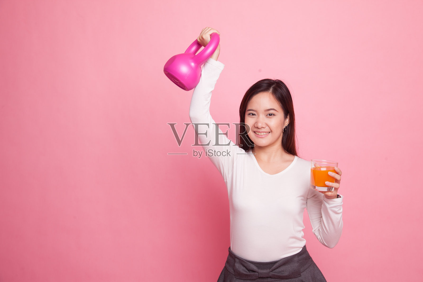 年轻的亚洲女人拿着哑铃喝橘子汁。照片摄影图片