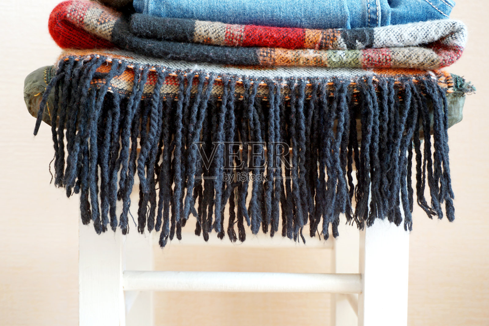 在一张白色的椅子上堆放着不同图案的波西米亚风格的保暖衣服。照片摄影图片