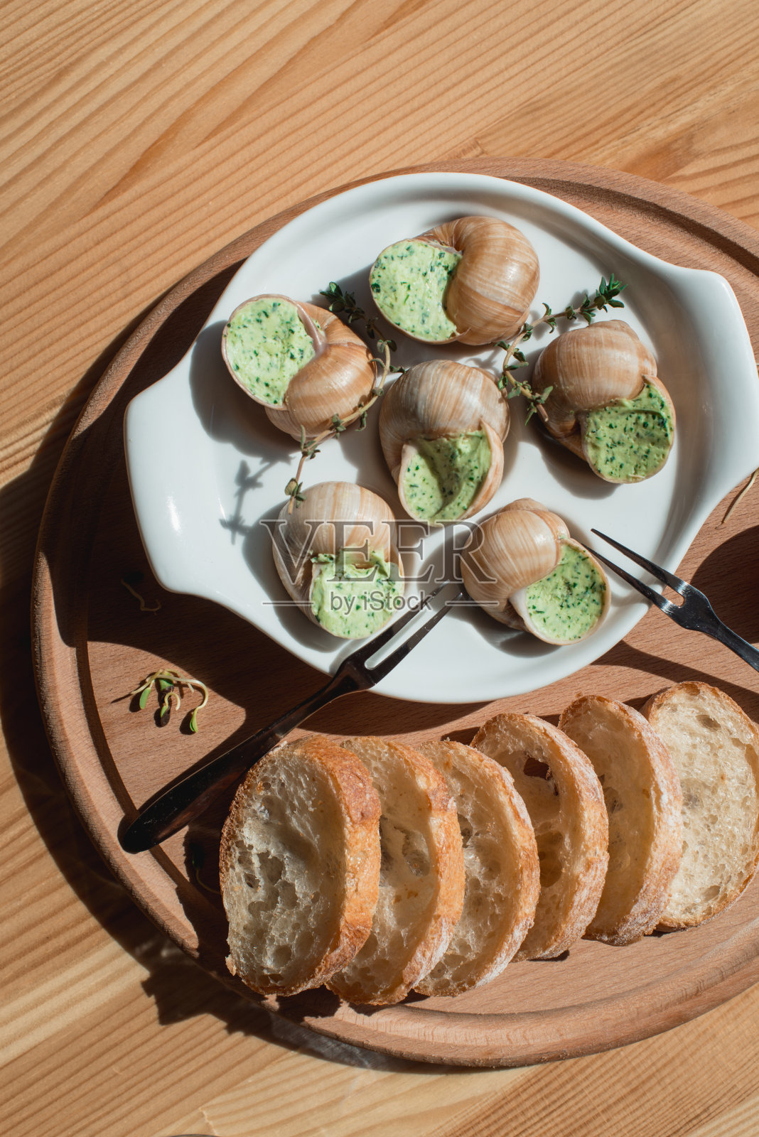 蜗牛与香草黄油，在传统的陶瓷平底锅面包在木板上。俯视图照片摄影图片