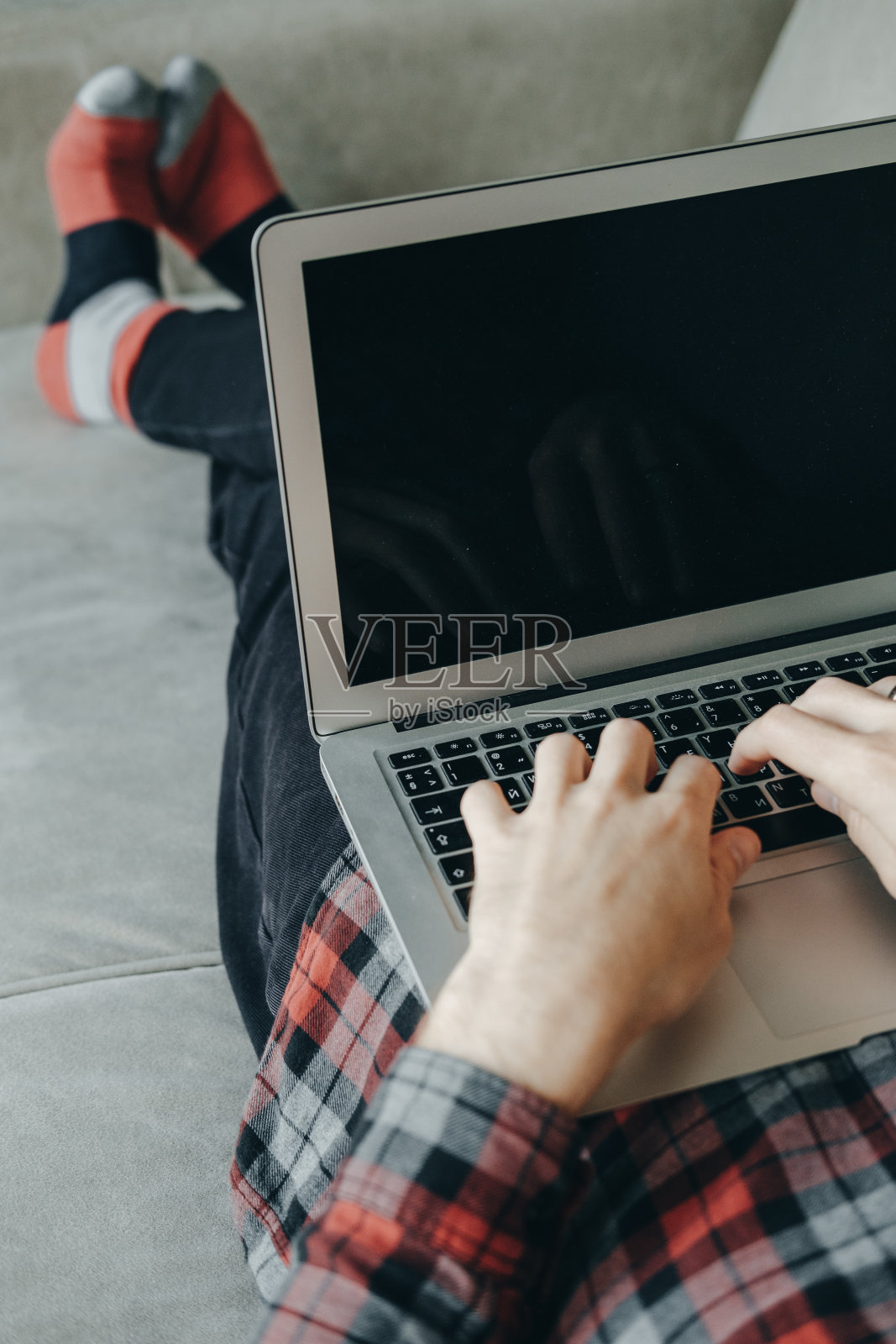 穿着红袜子躺在沙发上用笔记本电脑工作的嬉皮士照片摄影图片