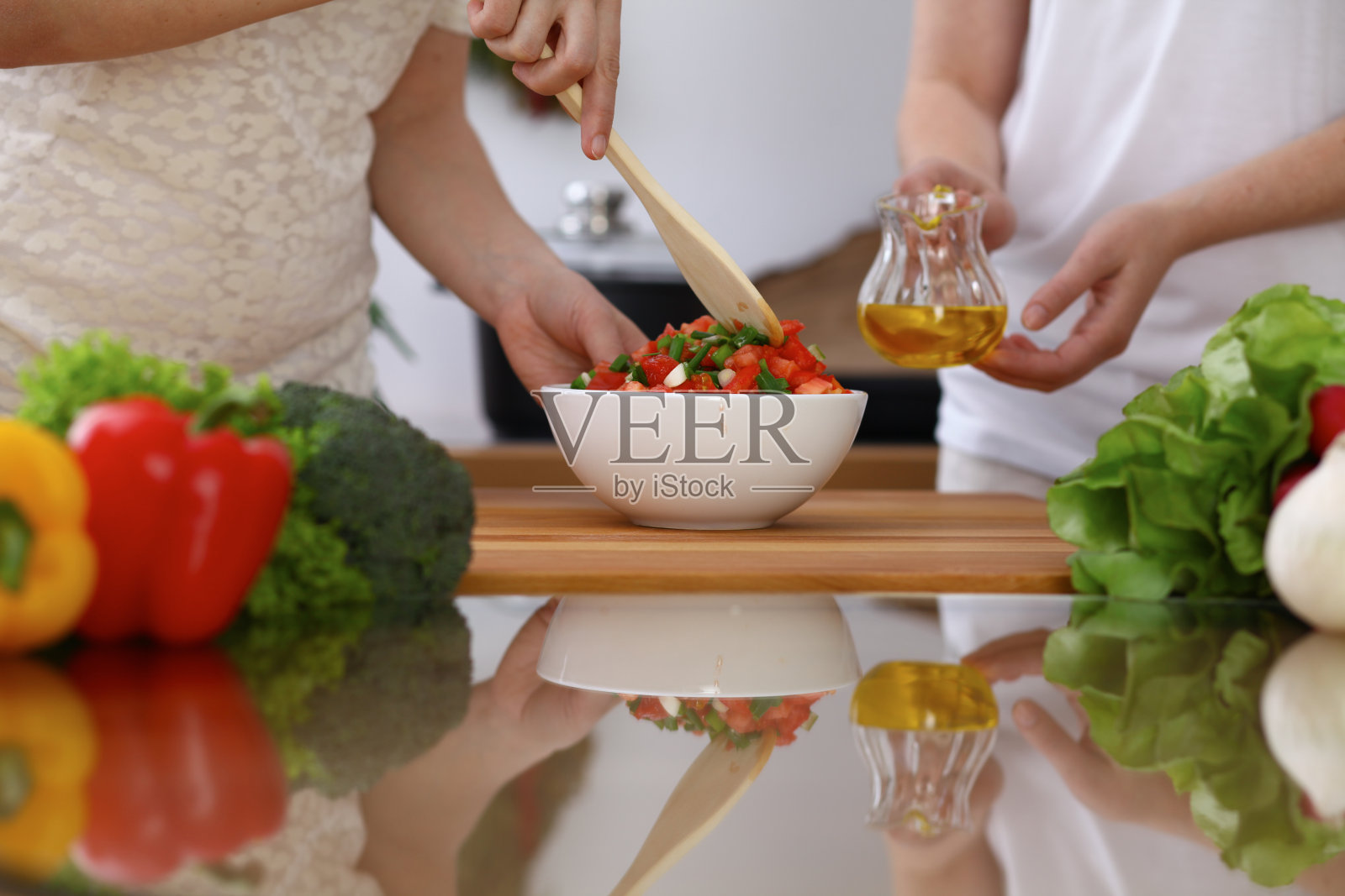 人类的手在厨房烹饪的特写。母亲和女儿或两个女性朋友混合蔬菜沙拉。健康饮食，素食和生活方式的概念照片摄影图片