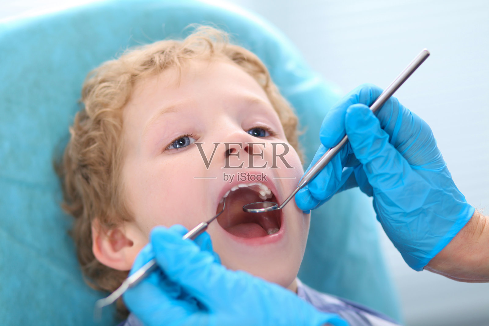 小卷毛男孩在牙科医生检查口腔时张大了嘴巴。照片摄影图片