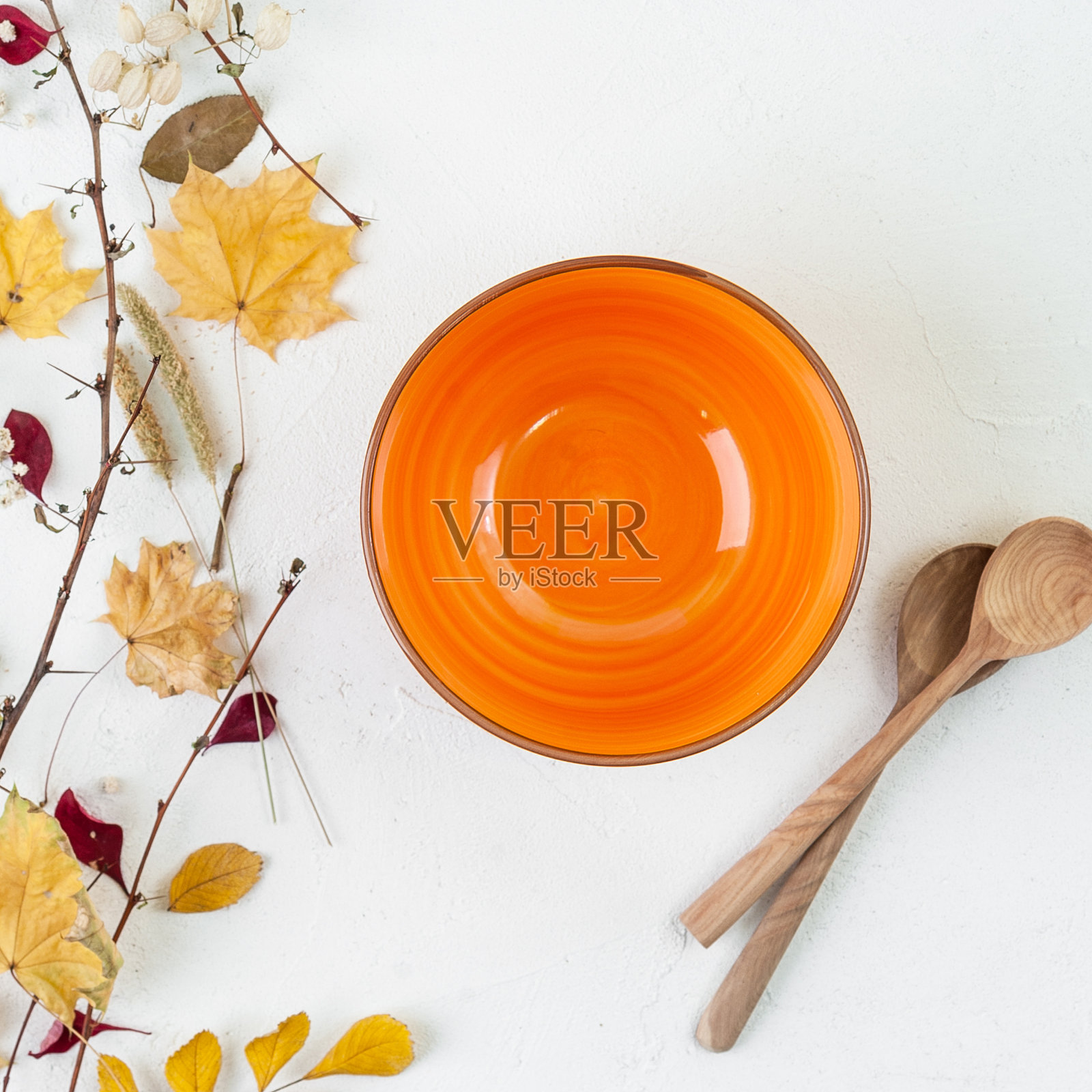 明亮的橙色空碗，木勺和秋叶在白色的背景上。照片摄影图片