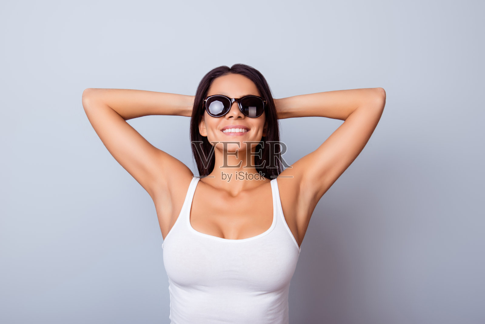 一个年轻的西班牙女孩的肖像，穿着休闲的衣服和太阳镜，站在蓝色的背景照片摄影图片