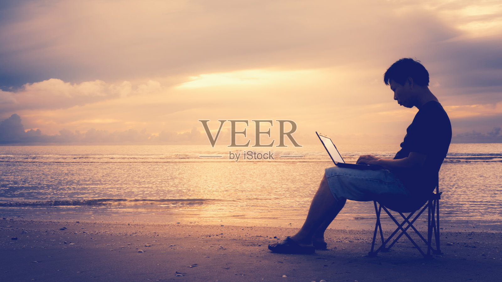 一个男人在海滩上用笔记本电脑。照片摄影图片