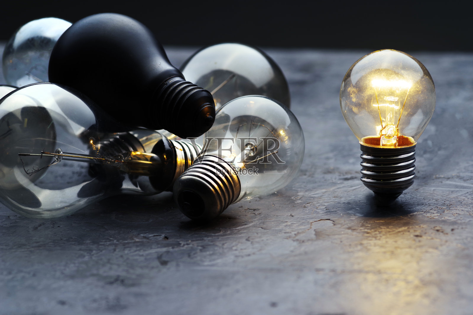 烧着灯泡，一个灯泡在灰色的混凝土背景上。照片摄影图片