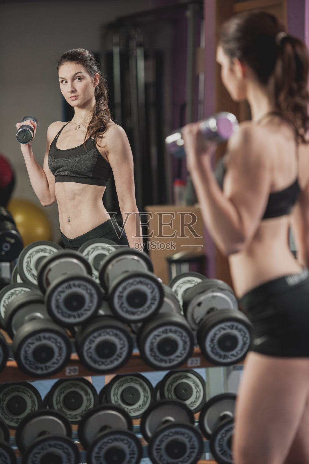 美丽健康的女人在健身房里用哑铃锻炼照片摄影图片