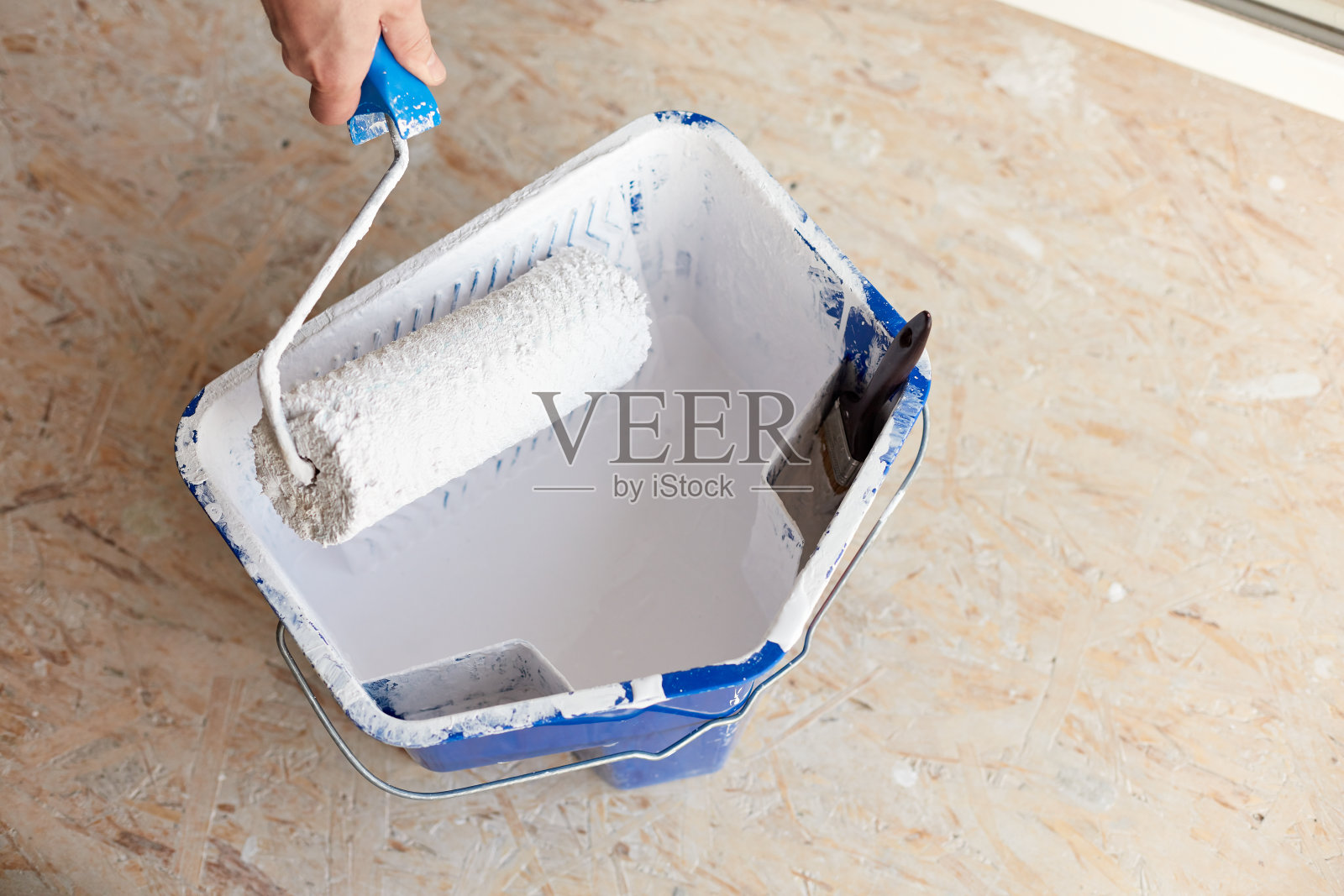 一桶白漆，一只男手拿着刷辊照片摄影图片