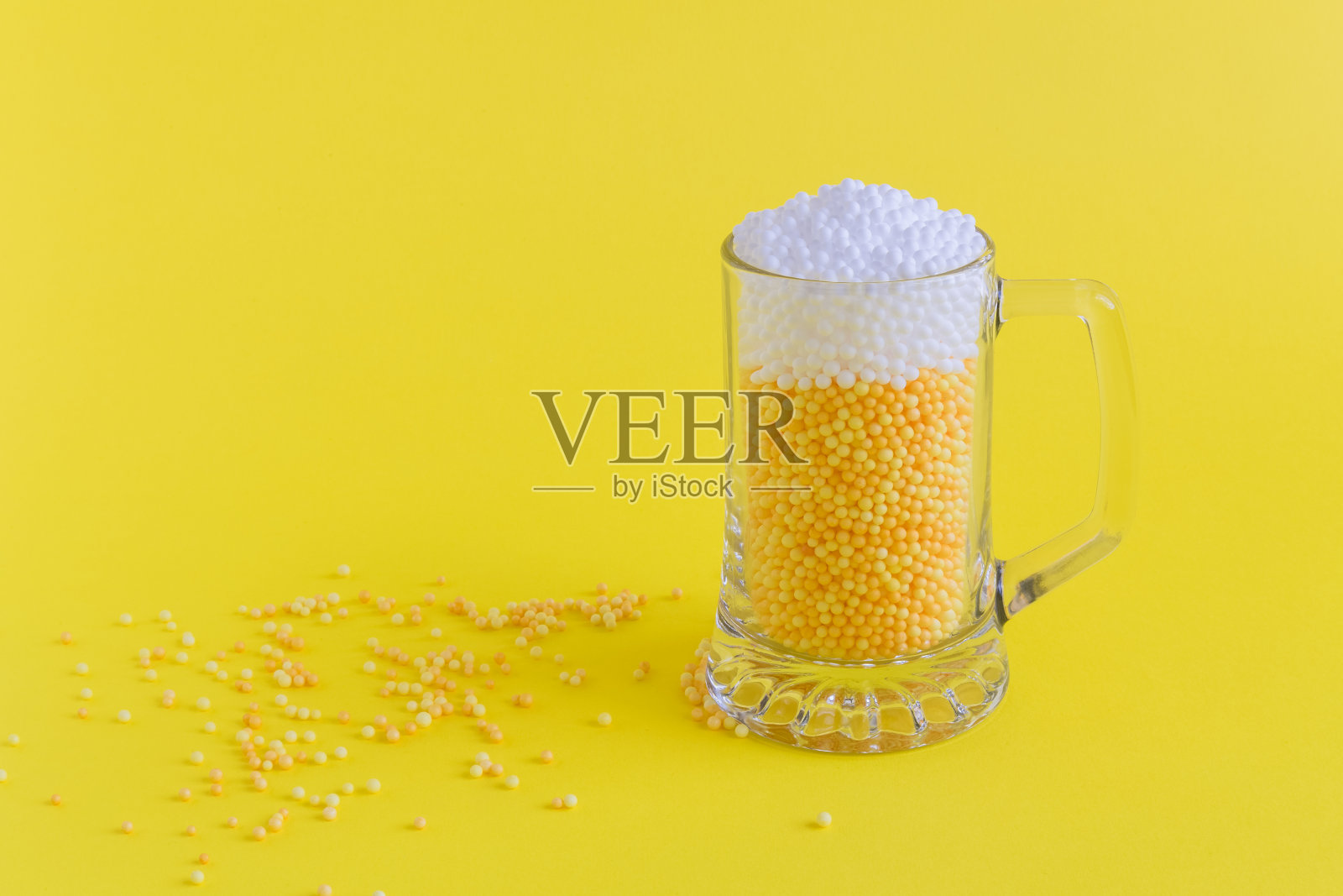 杯子里装满了黄色和白色的泡沫球，以啤酒的形式呈现简约的概念。照片摄影图片